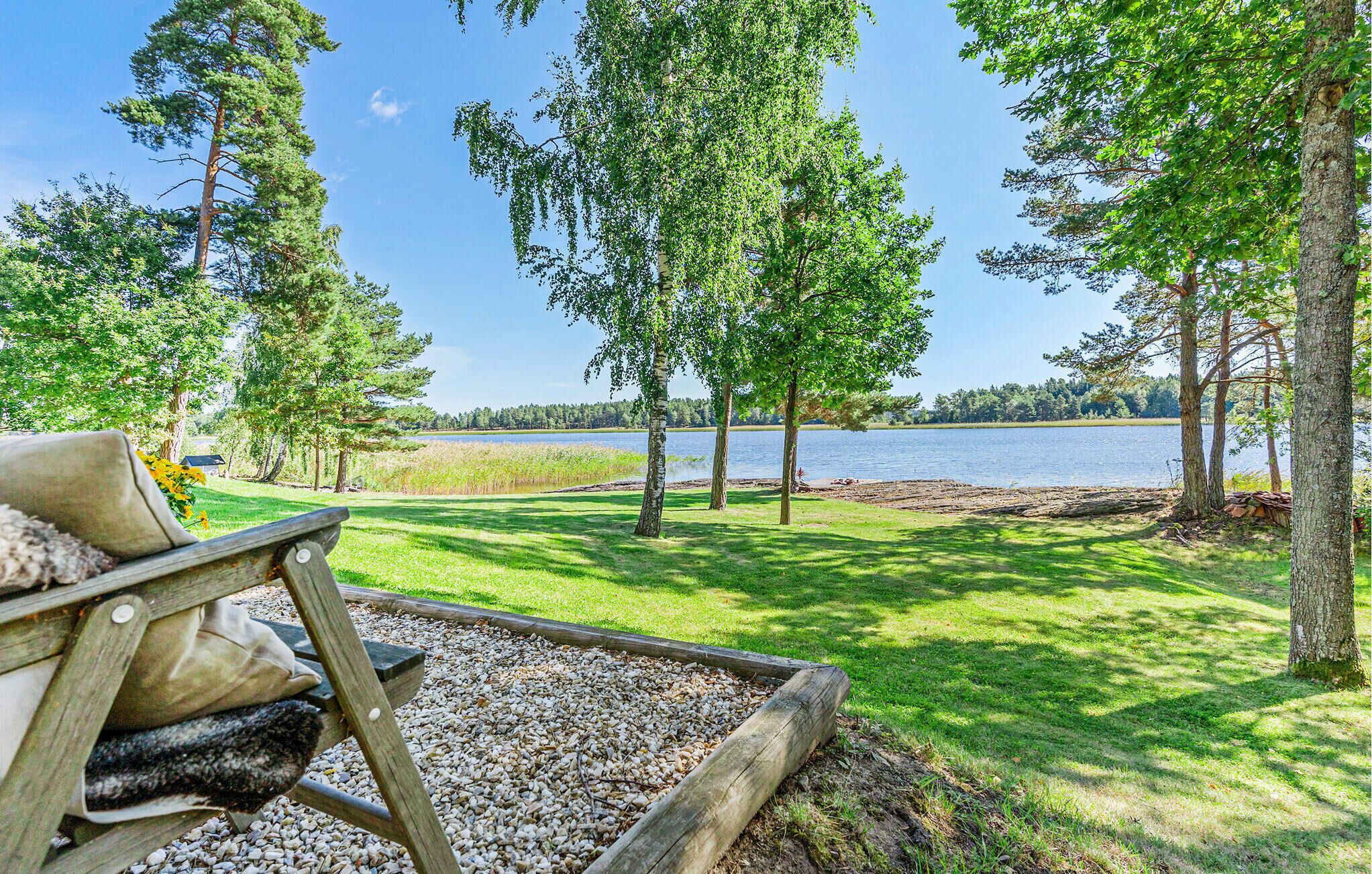 A lakeside view with a wooden deck, a fishing chair, and a gravel area.