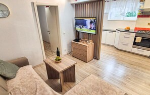Un espace de vie compact comprenant un canapé, une table basse en bois, un téléviseur et un coin cuisine avec des placards et une cuisinière.
