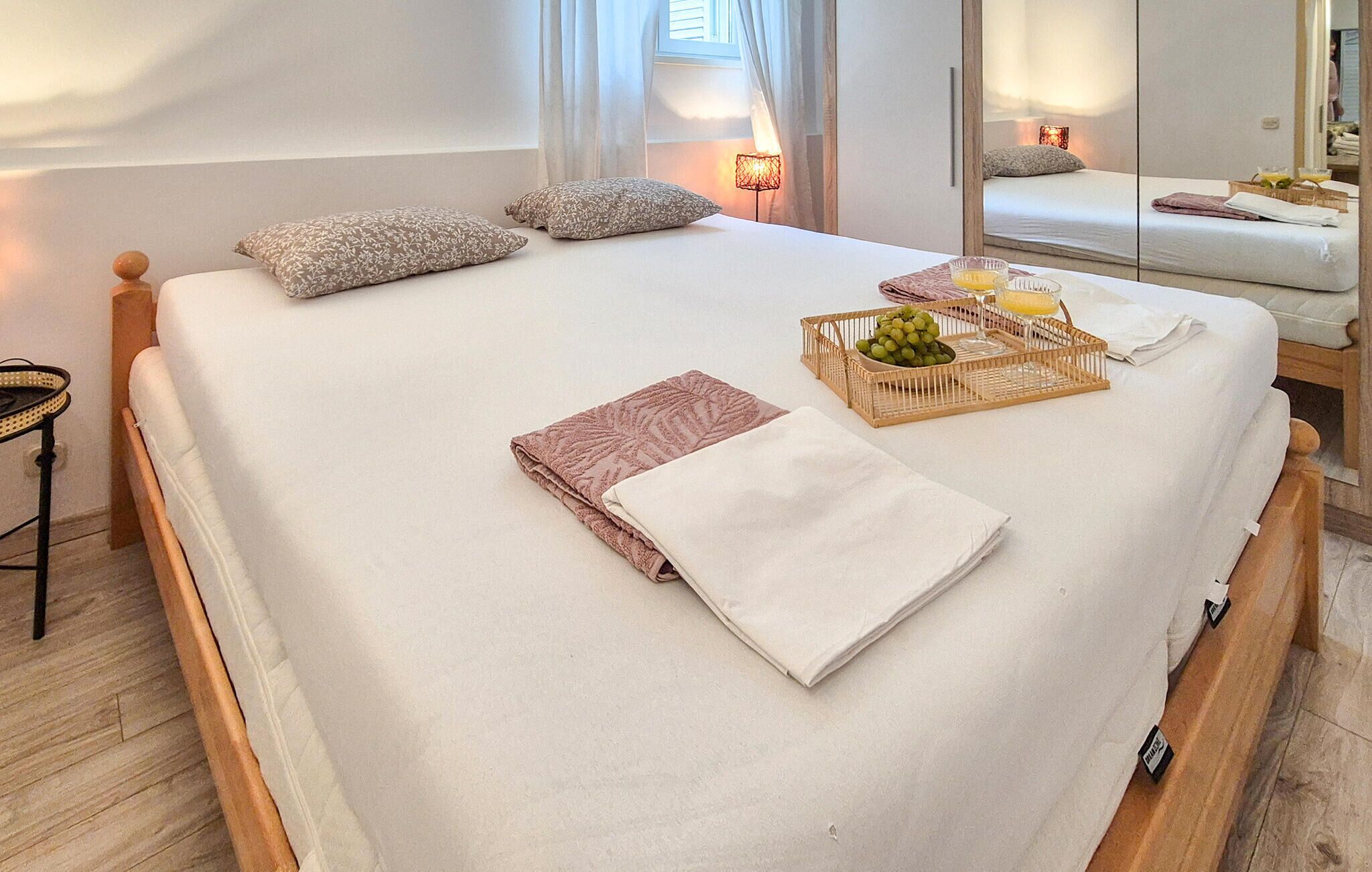 A neatly made bed with pillows, a bedside table with a lamp, and a fruit basket on the bed.