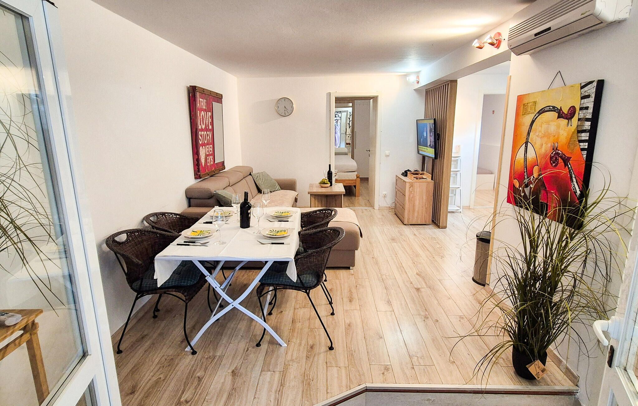 A dining area with a table set for four, a sofa, a TV, and a painting on the wall.