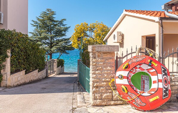 Une rue côtière bordée d’un mur de pierre, avec un objet gonflable rouge et un bâtiment doté d’un toit en tuiles.