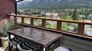 Un balcon avec une table et des chaises en bois, un pot de fleurs et une vue sur la montagne.
