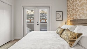 Une chambre avec un grand lit, deux portes donnant sur un balcon et un tableau encadré au mur.