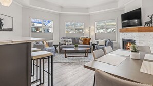 Un salon moderne doté d’une cheminée, de grandes fenêtres et d’un téléviseur à écran plat.