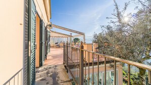 Un balcon doté d’une balustrade en métal, d’un sol carrelé et offrant une vue sur un jardin planté d’oliviers.