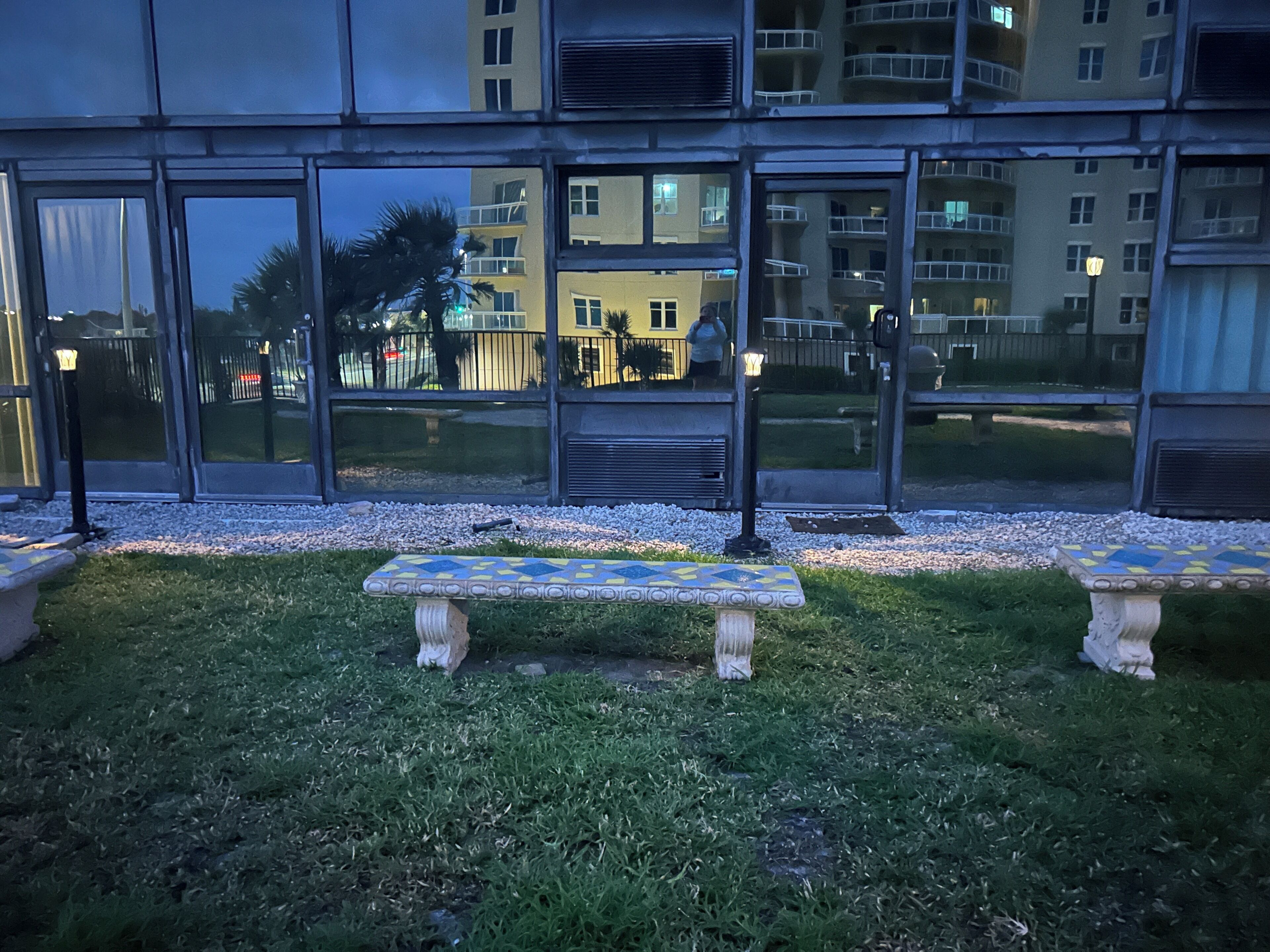 Un patio con dos bancos de piedra y una mesa con azulejos, rodeado por un muro de piedra bajo y un área con césped.