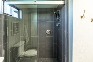 Eine moderne Dusche mit Glastür, einer sichtbaren Toilette und einer an der Wand befestigten Duschbrause.