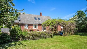 Une maison en briques rouges, avec un toit gris, une petite fenêtre et une clôture en bois.