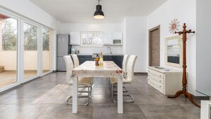 Eine moderne Küche mit weißen Schränken, einem Essbereich mit Tisch und Stühlen und einem großen Fenster, das für natürliches Licht sorgt.