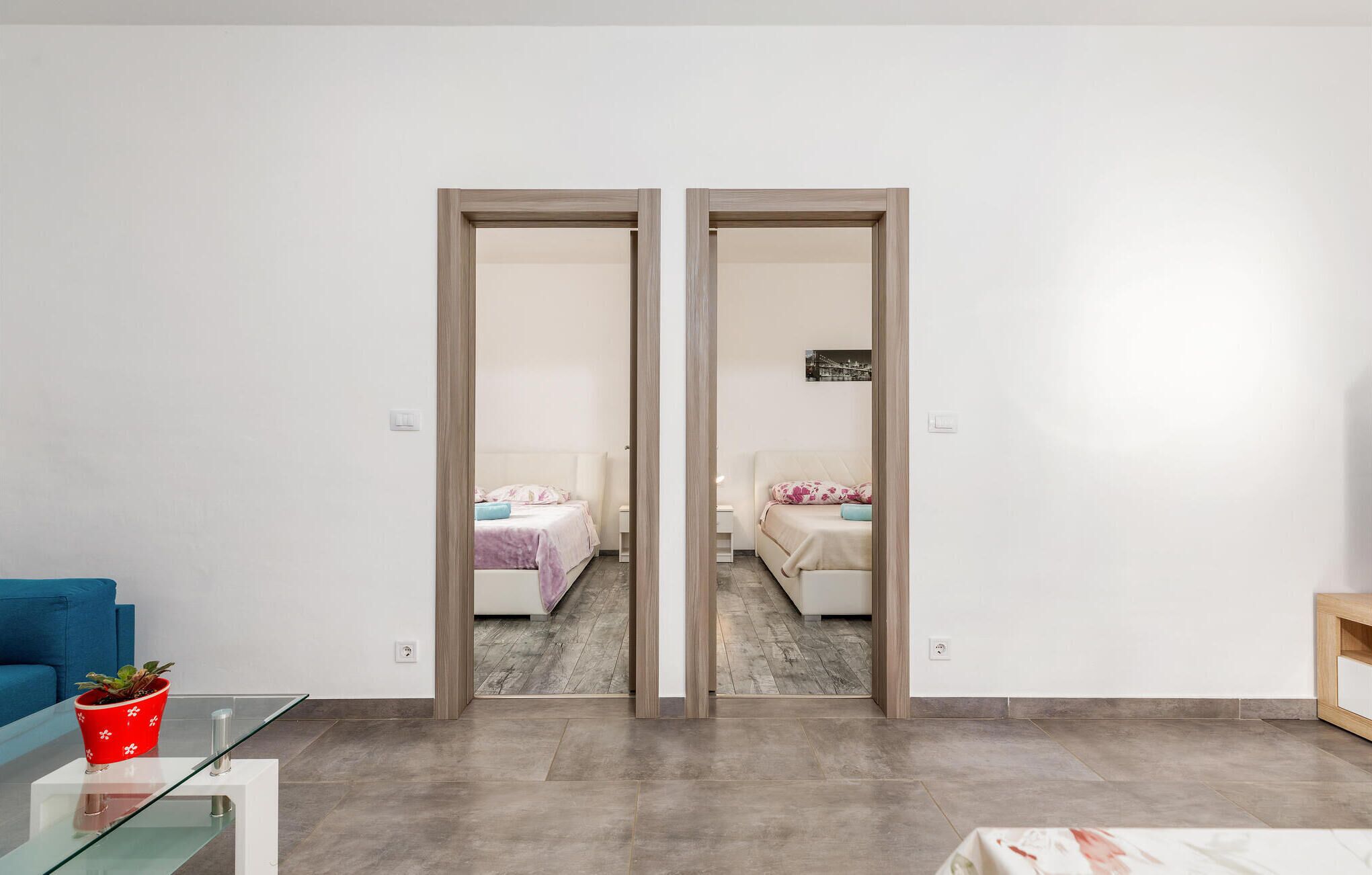 Una habitación moderna con un armario espejo, un sofá azul, una mesa de centro de vidrio y una pequeña mesa con una maceta roja.
