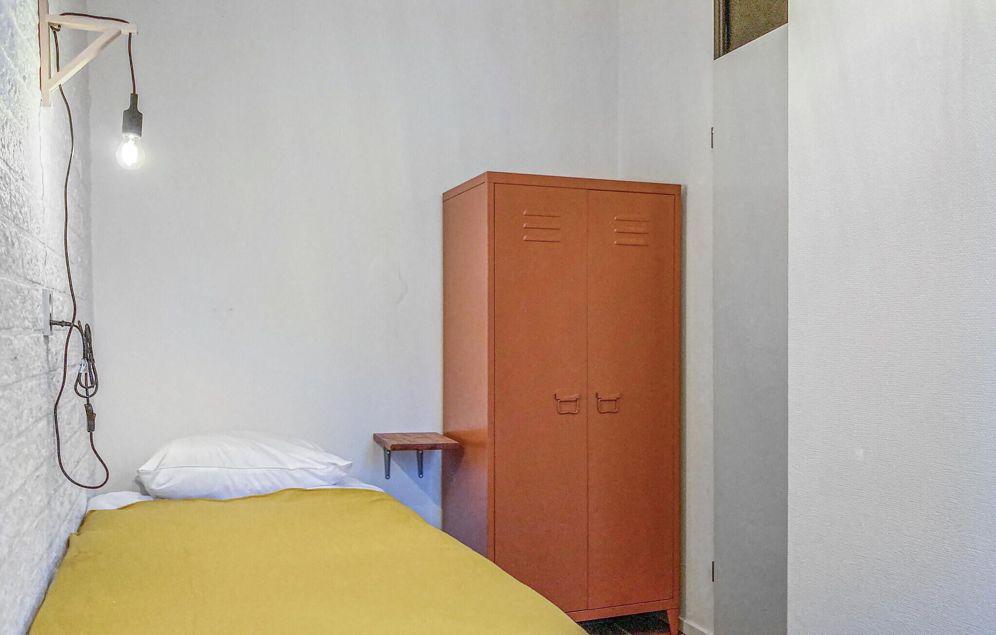 Une petite chambre avec un lit simple, une armoire en bois, une table de chevet et un luminaire fixé au mur.