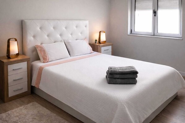 A neatly made bed with a tufted headboard, bedside tables with lamps, and a window with blinds.