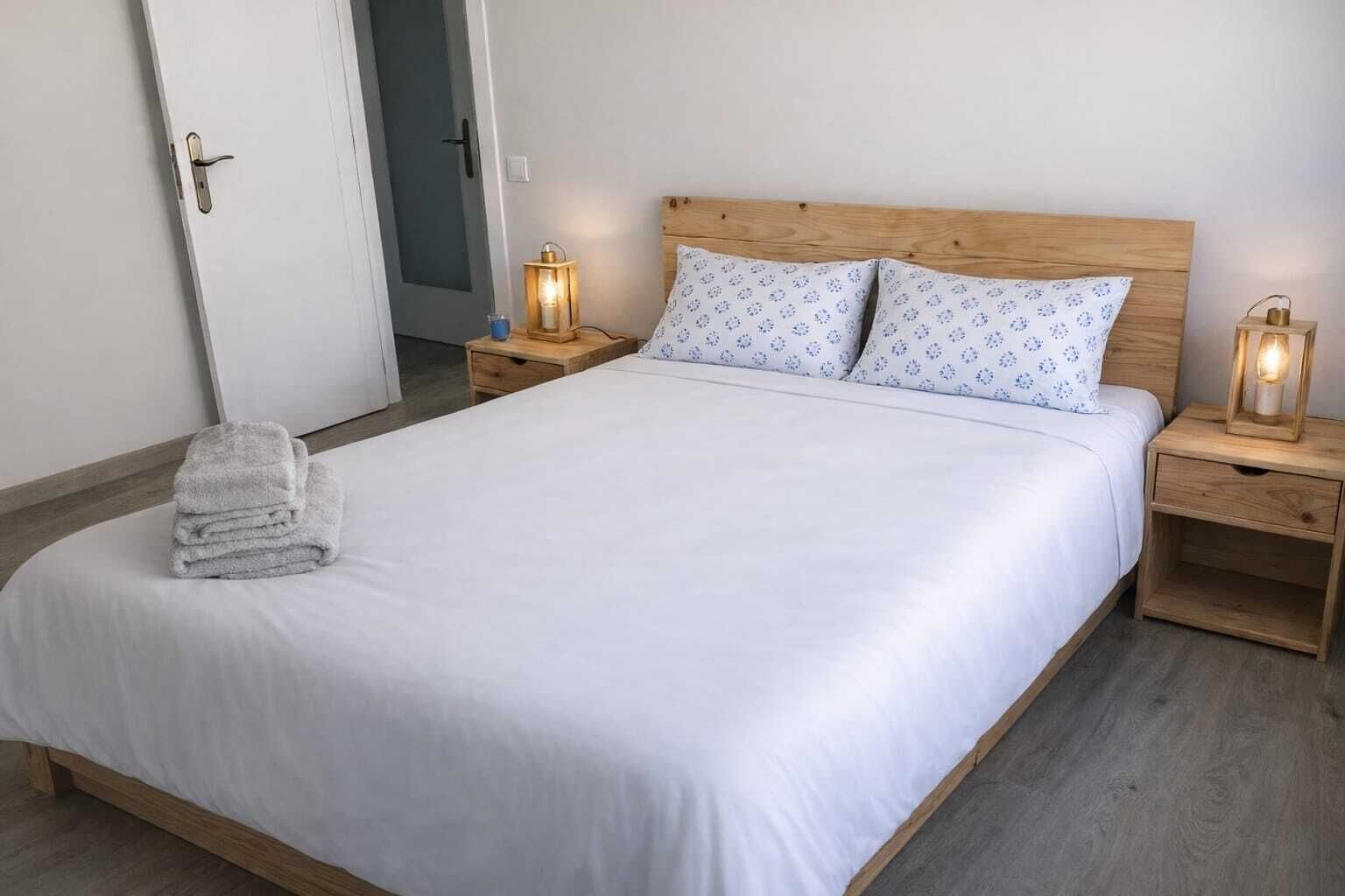 Una cama bien hecha con ropa blanca, dos almohadas con un diseño azul y dos mesitas de noche con lámparas.