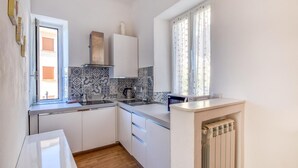 A compact kitchen with white cabinets, a patterned backsplash, a window with curtains, and a built-in radiator. - 1 bedroom stunning apartment in Varazze (Varazze)