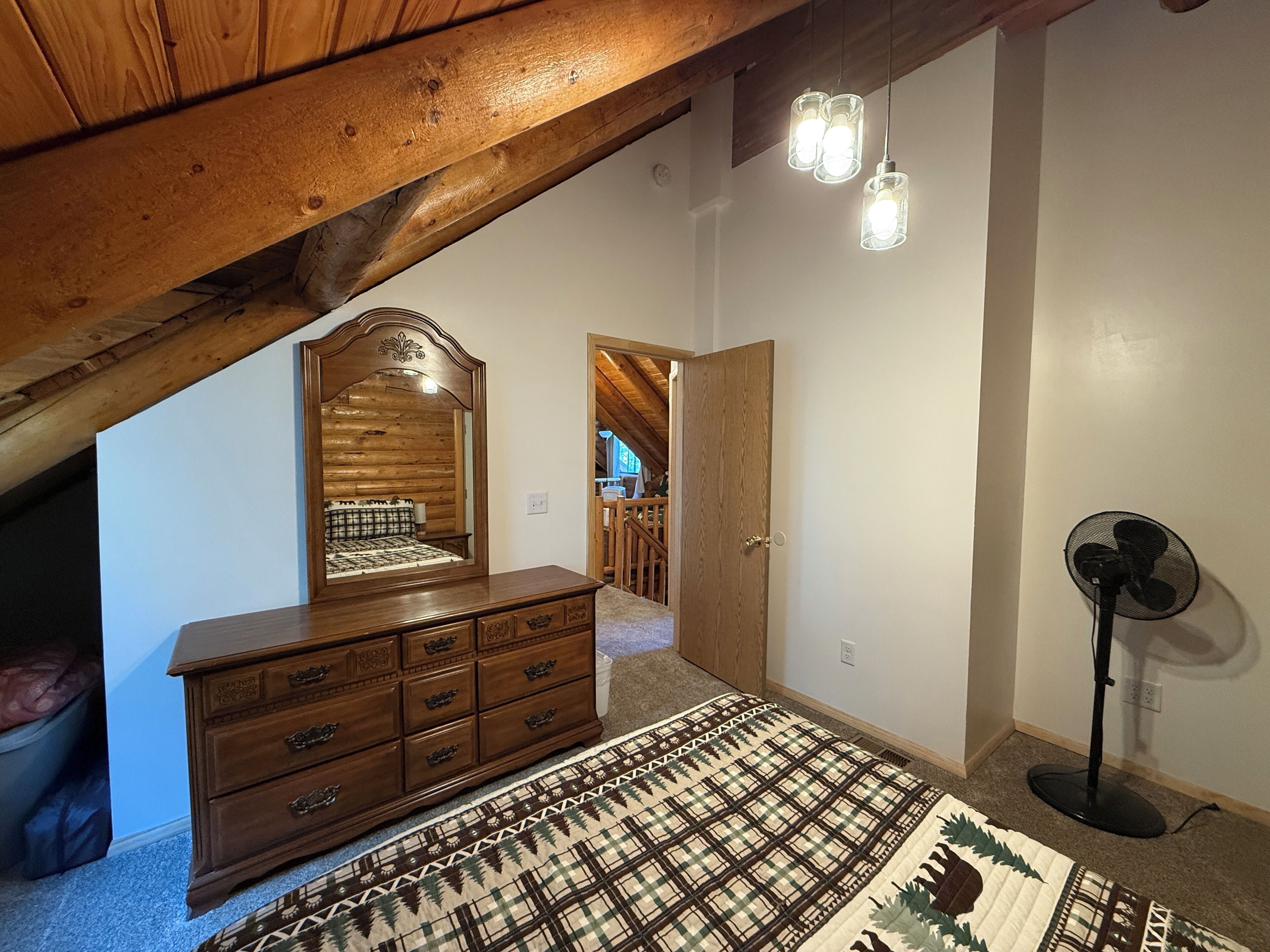 Een kamer met een houten dressoir, een kamerbreed tapijt, een spiegel en een ventilator.