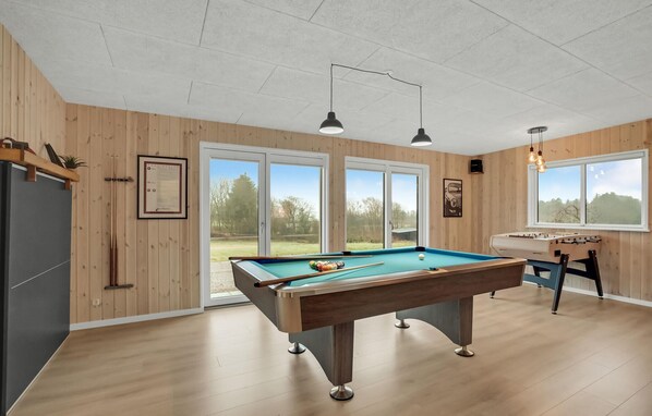 Een pooltafel in een ruimte met houten wanden, een groot raam en een tafelvoetbal.