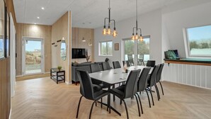 Uma área de jantar moderna com uma mesa grande, cadeiras pretas e iluminação pendente.