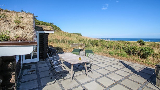 En terrasse med et bord og stole, en stenvæg og havudsigt.
