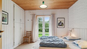 Un dormitorio con techo de madera, un ventanal con cortinas, una cama con ropa de cama azul y una silla.