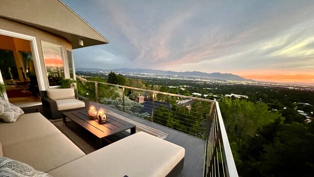 Un balcón con sofá y mesa, con vistas a un paisaje urbano al atardecer.