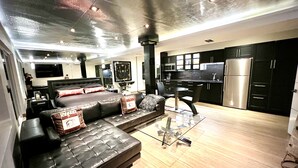 Una sala de estar moderna con un sofá de cuero negro, una mesa de centro de vidrio y un comedor con una silla negra y una pequeña mesa.