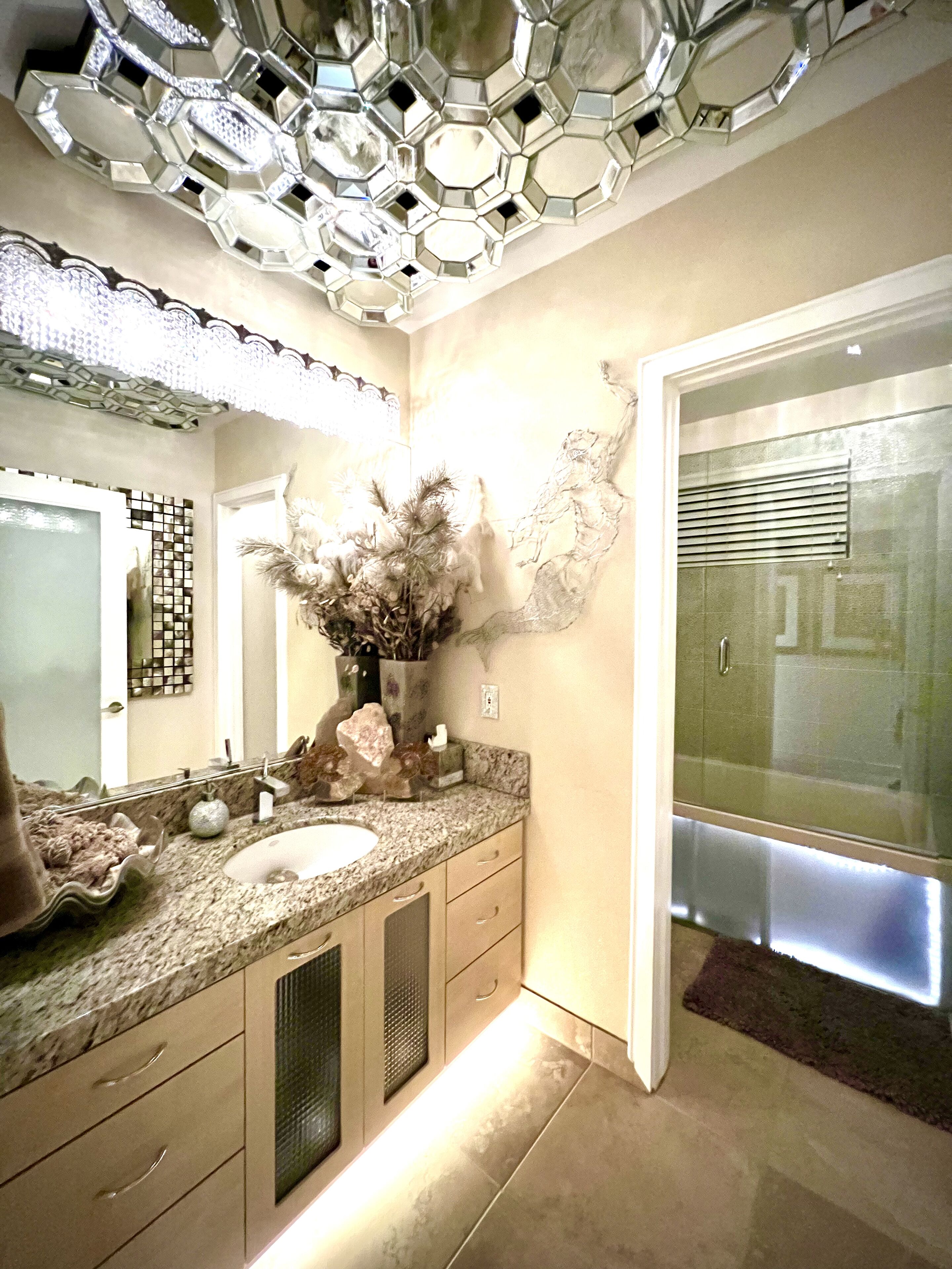 A modern bathroom with a large mirror, two sinks, a decorative vase, and a shower area.