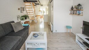 A modern living room with a grey sofa, a white coffee table, and a TV on a white stand. There is a staircase leading to an upper level, and a bookshelf with books and decorative items. - Lovely apartment in Samsø (Samsø)