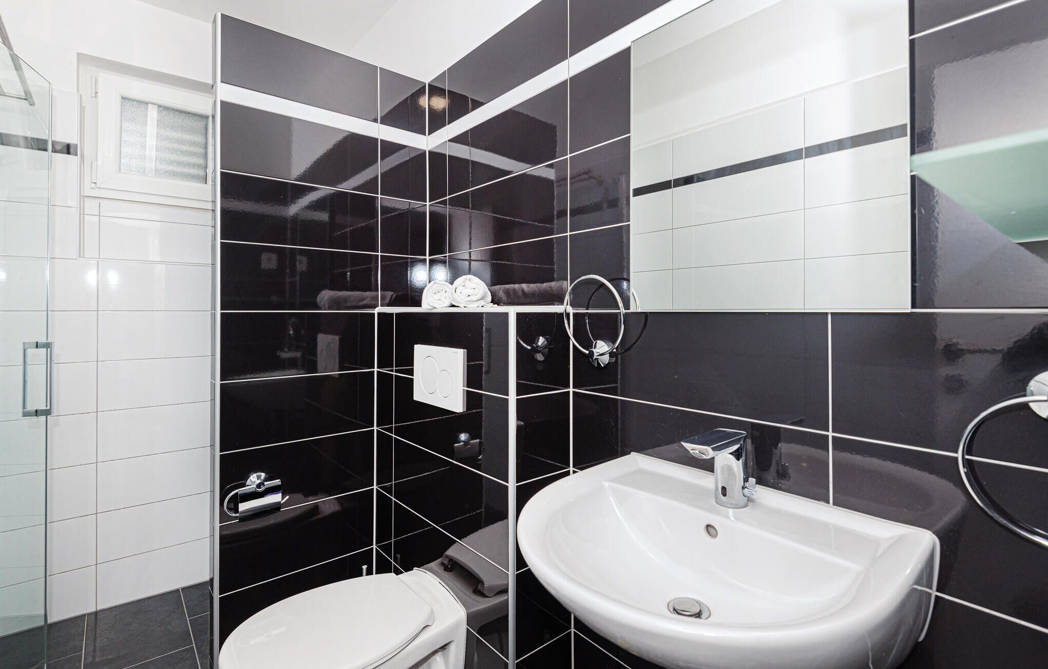 Ein modernes Badezimmer mit einem weißen Waschbecken, einer Toilette und einer Duschkabine aus Glas.