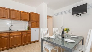 Cozinha moderna com armários de madeira, lava-louças embutida e área de jantar com mesa de vidro e cadeiras brancas.