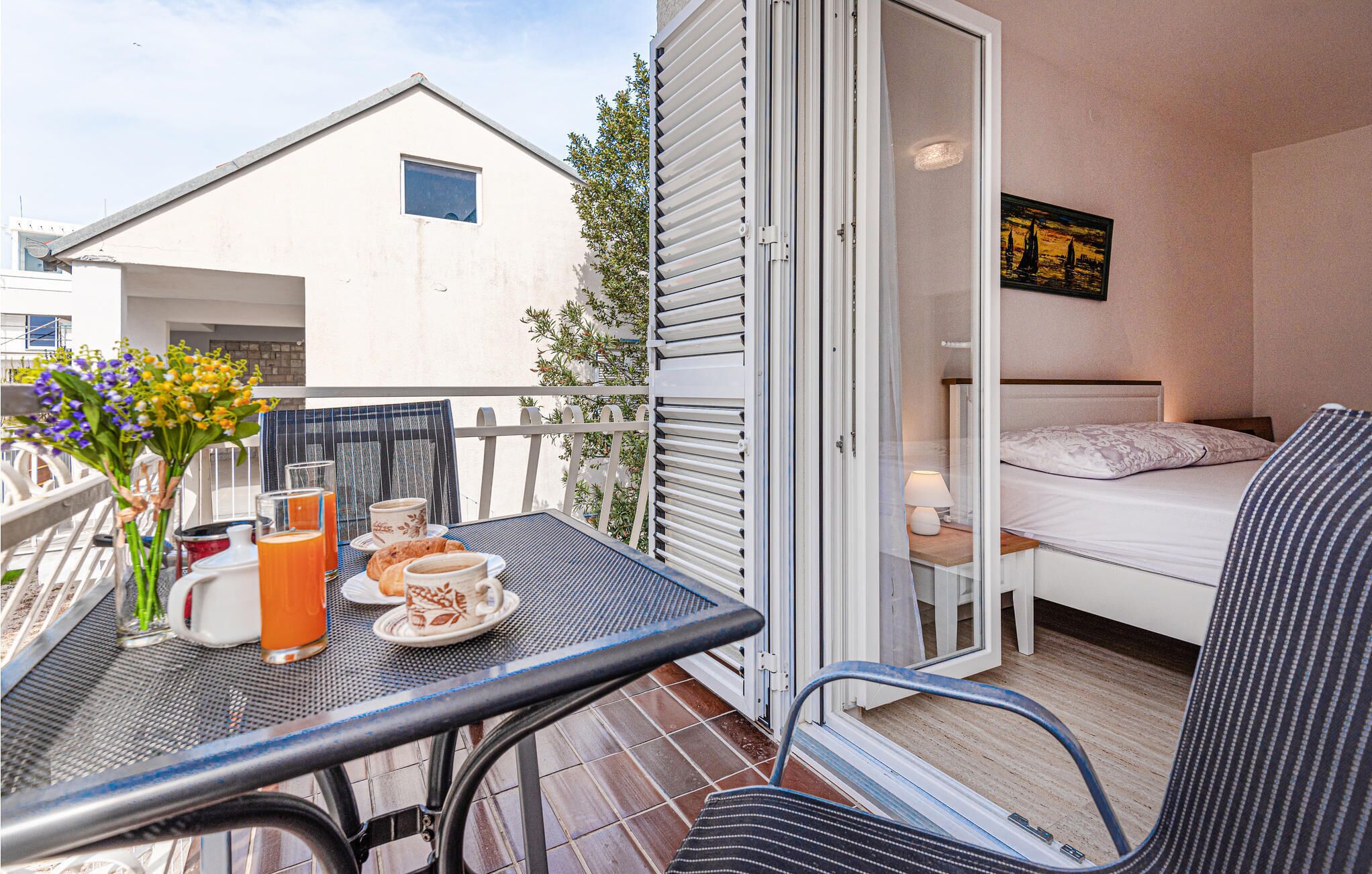 A balcony with a table set for breakfast, a bed with a view, and a small window.