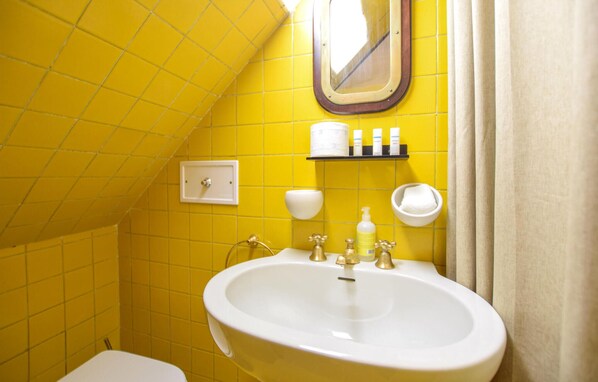 A bathroom with yellow tiled walls, a white sink, a mirror, and toiletries on a shelf.
