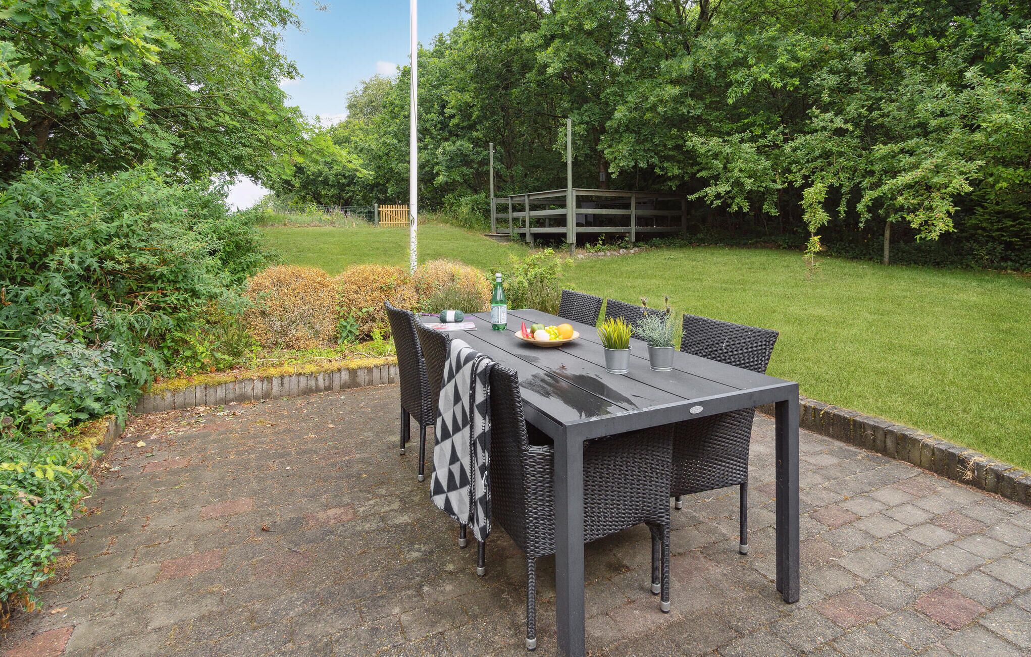 Une terrasse extérieure avec une table et des chaises, entourée de verdure et d’une clôture en bois.