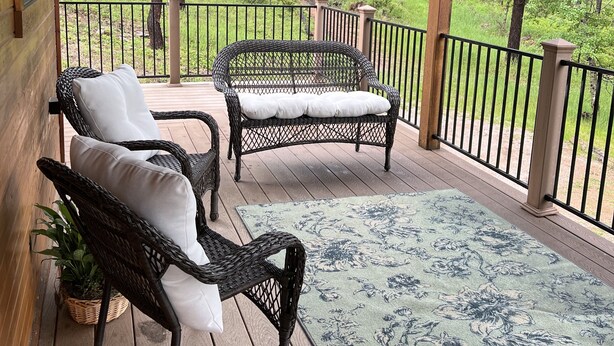 A covered porch with wicker furniture and a floral rug, overlooking a forested area. - Cozy cabin in the beautiful Black Hills (Newcastle)