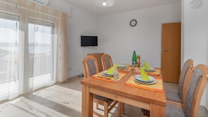Ein Essbereich mit einem Holztisch, gedeckt für zwei Personen, Stühlen, einem an der Wand montierten Fernseher und einer Glastür zum Balkon.