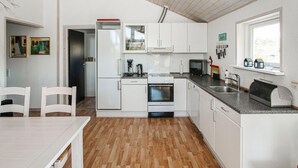 A compact kitchen with white cabinets, a built-in oven, a microwave, and a sink. There is a window providing natural light and a door leading to another room. - 2 bedroom nice home in Samsø (Samsø)