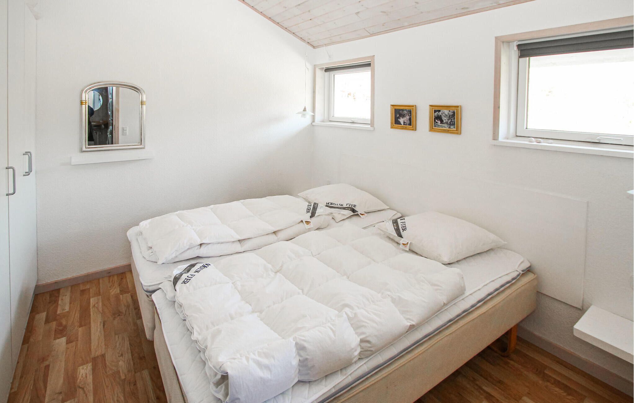 A bedroom with a bed, a window, and a small shelf with framed pictures.