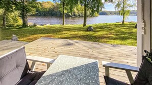 A deck with outdoor seating, overlooking a lake and surrounded by trees. - Nice home in Tjörnarp (Tjörnarp)