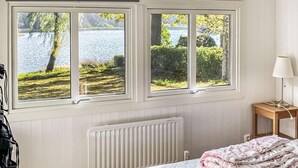 A bedroom with a view of a lake, a radiator, a bedside table with a lamp, and a bed with a floral blanket. - Nice home in Tjörnarp (Tjörnarp)