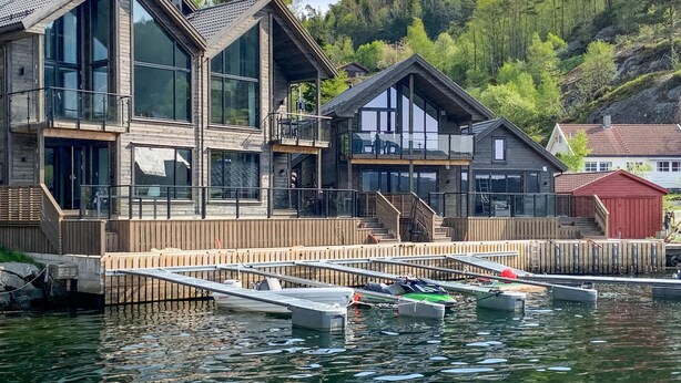 A modern waterfront property with large glass windows, wooden decks, and docked boats.