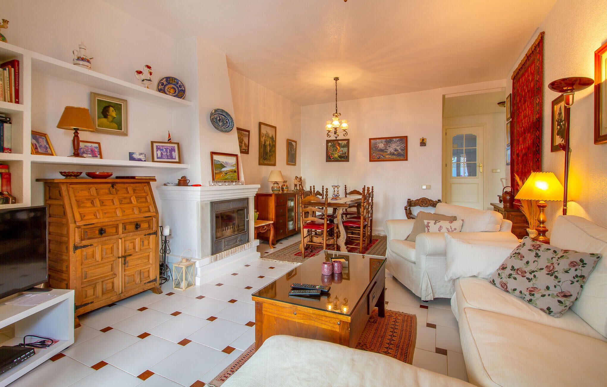 A cozy living room with a fireplace, white sofas, a wooden cabinet, and various decorative items on shelves.