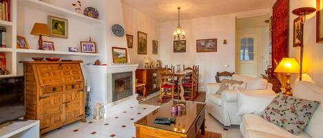 A cozy living room with a fireplace, white sofas, a wooden cabinet, and various decorative items on shelves.
