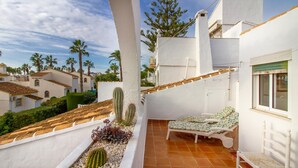 A rooftop terrace with a white chair, a small cactus, and a tiled floor.