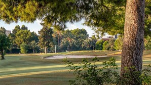 A golf course with a sand bunker, trees, and a clear sky.