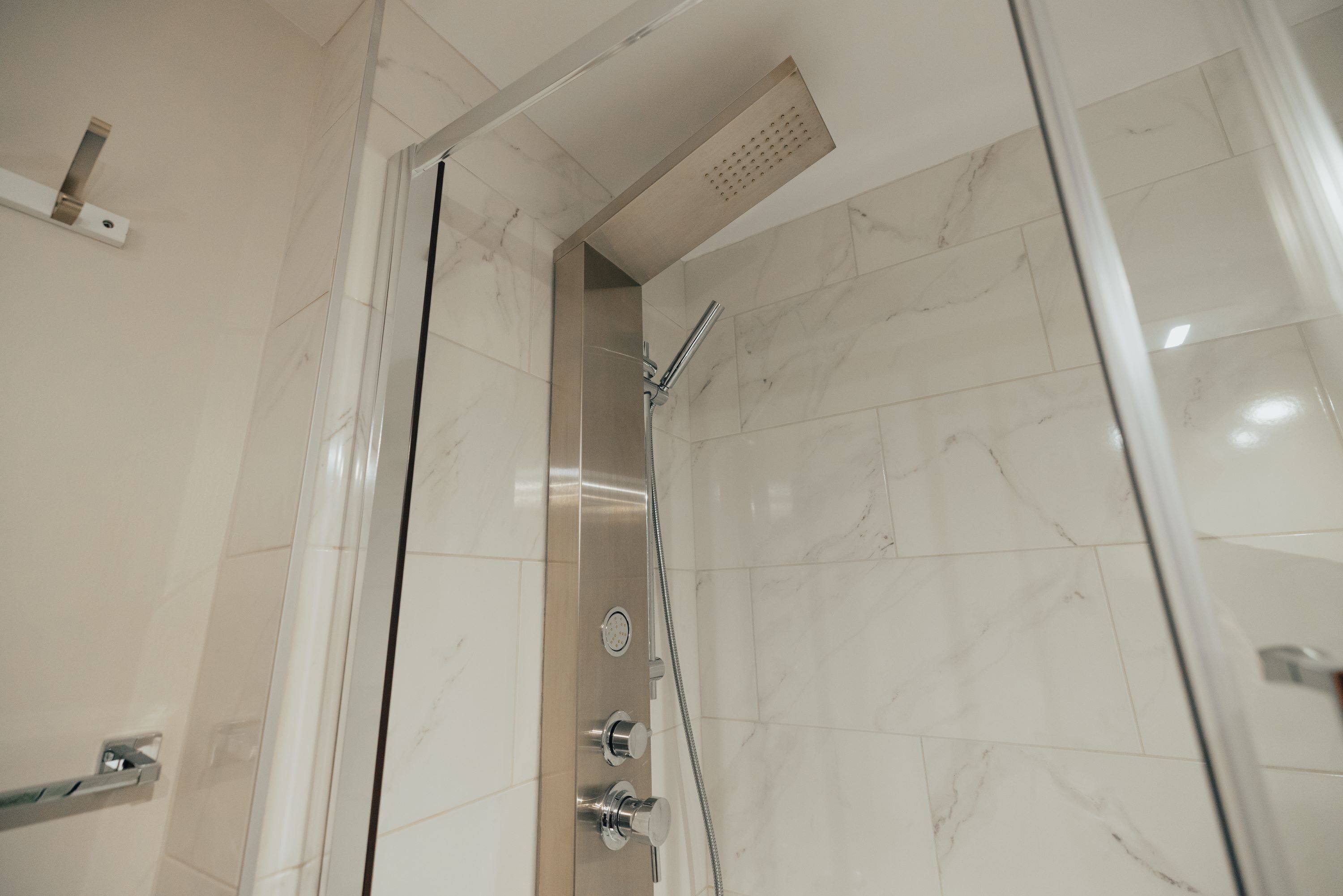 Ein modernes Badezimmer mit Duschkabine aus Glas, Marmorfliesen und einer sichtbaren Dusche.