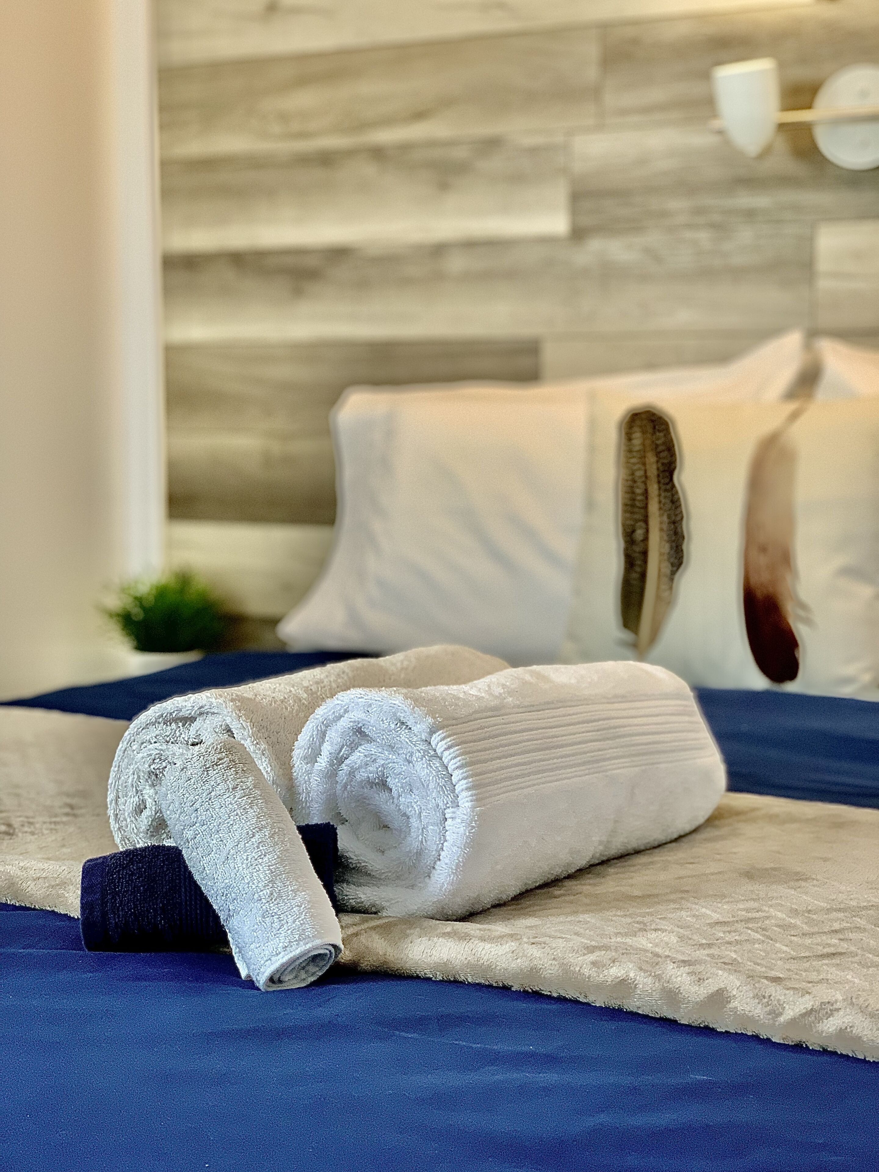 Een net opgemaakt bed met een blauwe sprei, witte handdoeken en een houten hoofdbord.