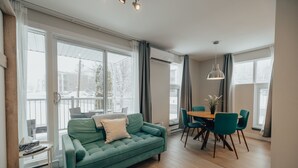 Un salon moderne avec un canapé vert, une table à manger avec des chaises et de grandes fenêtres.