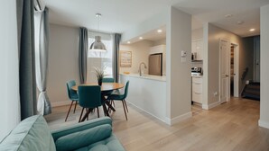 Un salon moderne avec un canapé de couleur turquoise, un coin repas avec une table ronde et des chaises, une cuisine avec des meubles blancs et un escalier menant à un autre niveau.