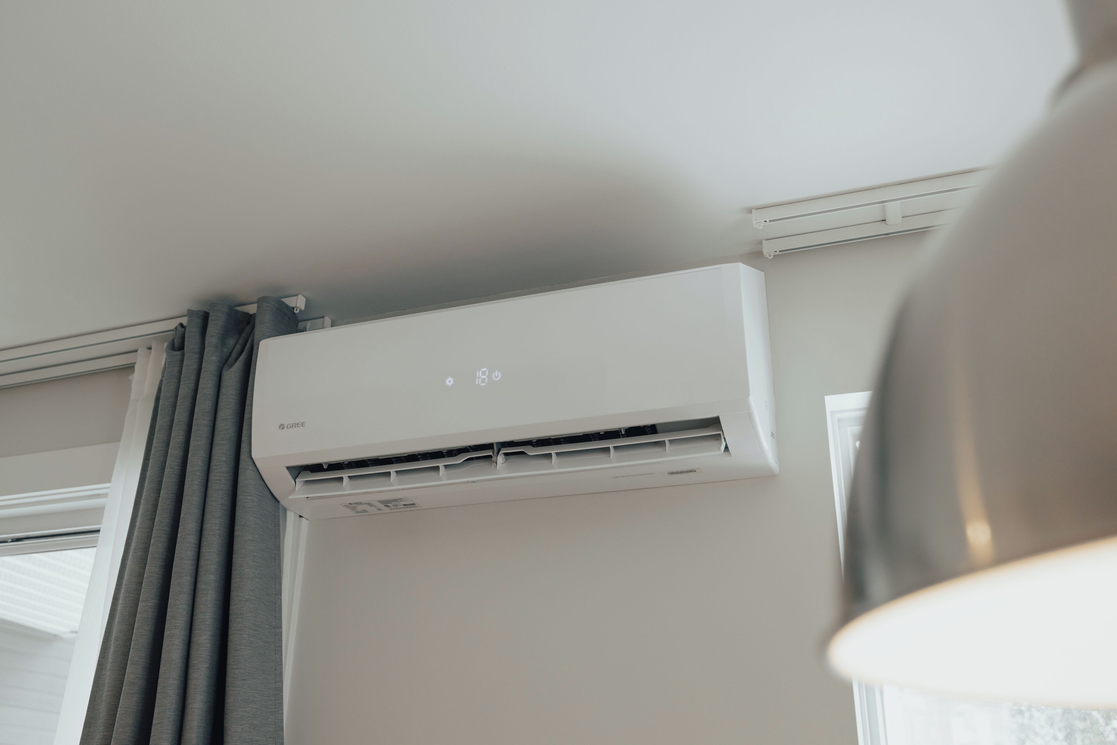 A white air conditioning unit mounted on a wall with a window and curtains.
