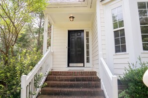 A white house with a black front door, a small porch, and a brick staircase.