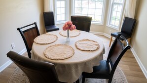 A dining table with a white tablecloth, four placemats, and a vase with pink flowers. - New modern kitchen in great location to RDU and RTP (Morrisville)